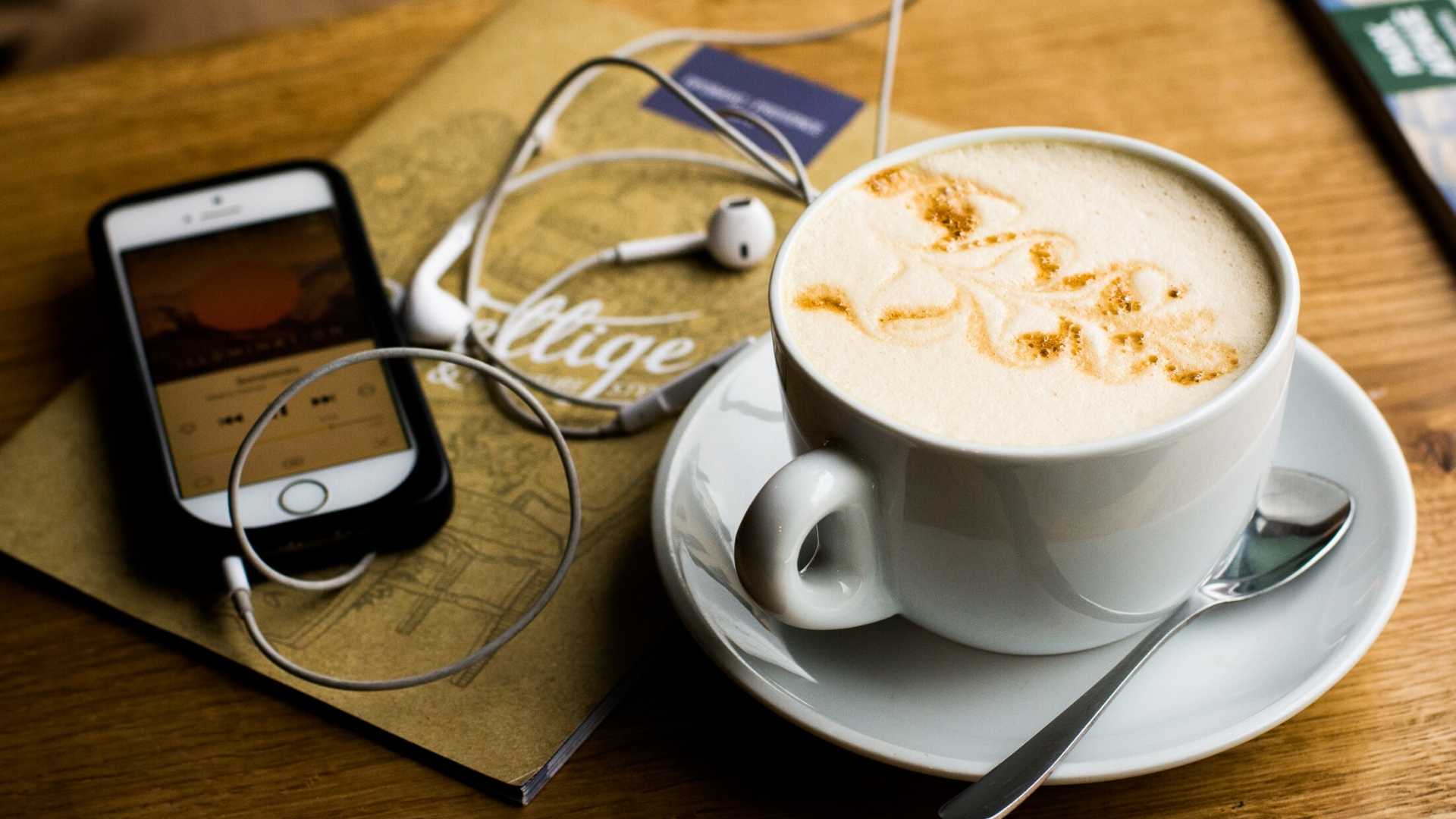 Téléphone jouant un podcast pour apprendre l'anglais posé à côté d'un café
